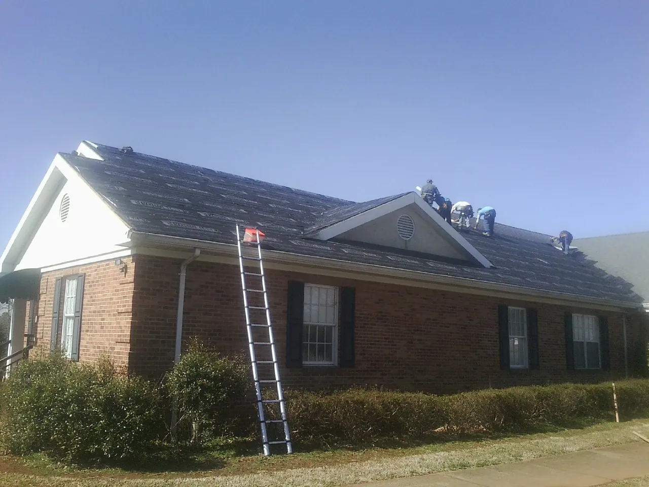 Crew tearing shingles off a brick ranch roof with a ladder set — Metal Roof Repair work by our crew in Saint Paul Park