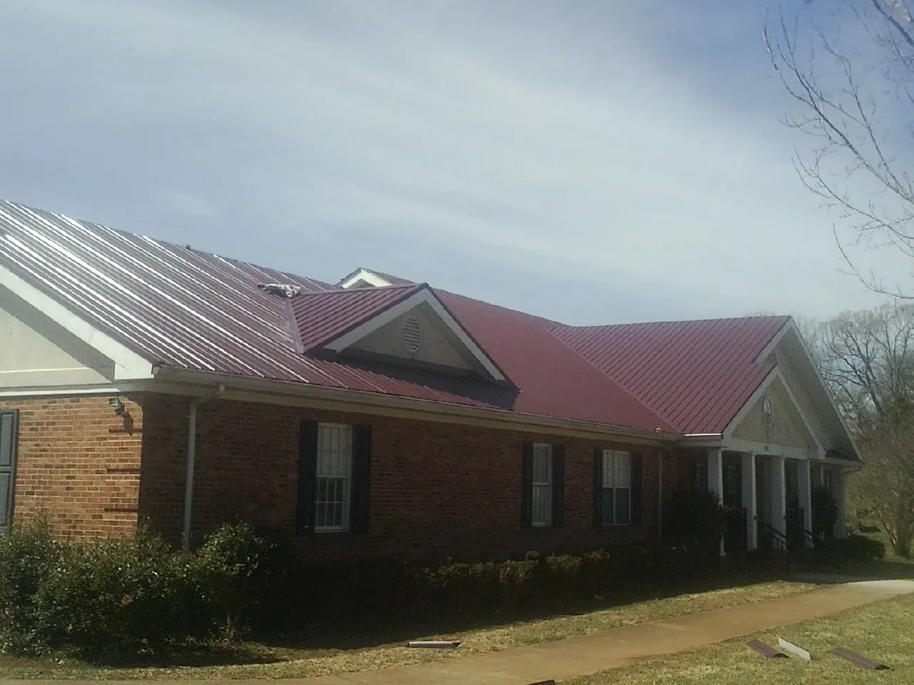 Red metal roof with gabled entries on a long brick building, from a Hail Damage Roof Repair job in Saint Paul Park
