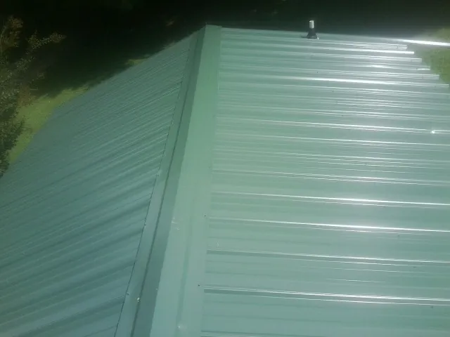 New green metal panels meeting at the ridge of a roof — Flat Roof Repair work by our crew in Saint Paul Park