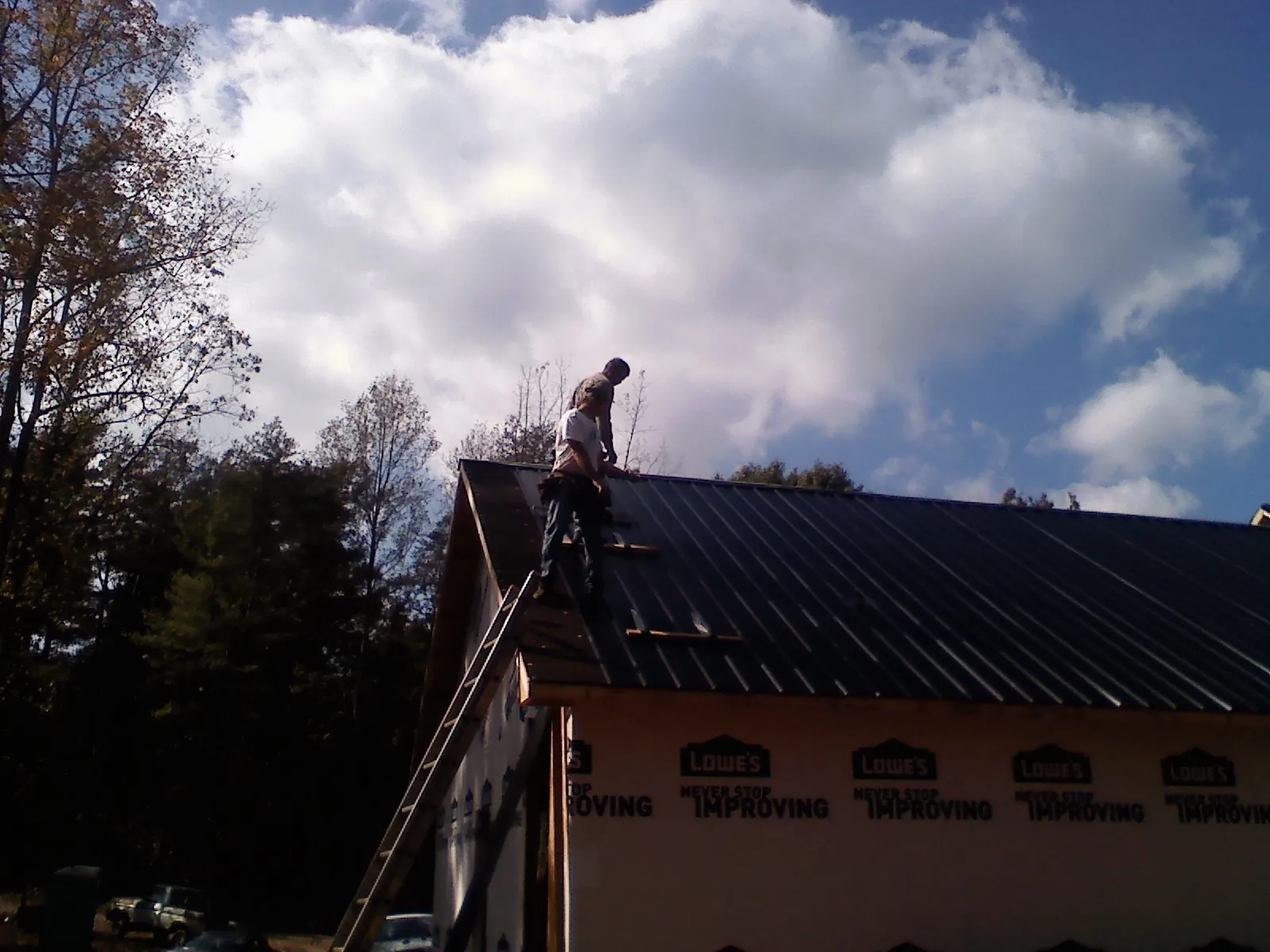 Roofer fastening dark metal panels high against a cloudy sky, from a Roof Inspection job in Saint Paul Park
