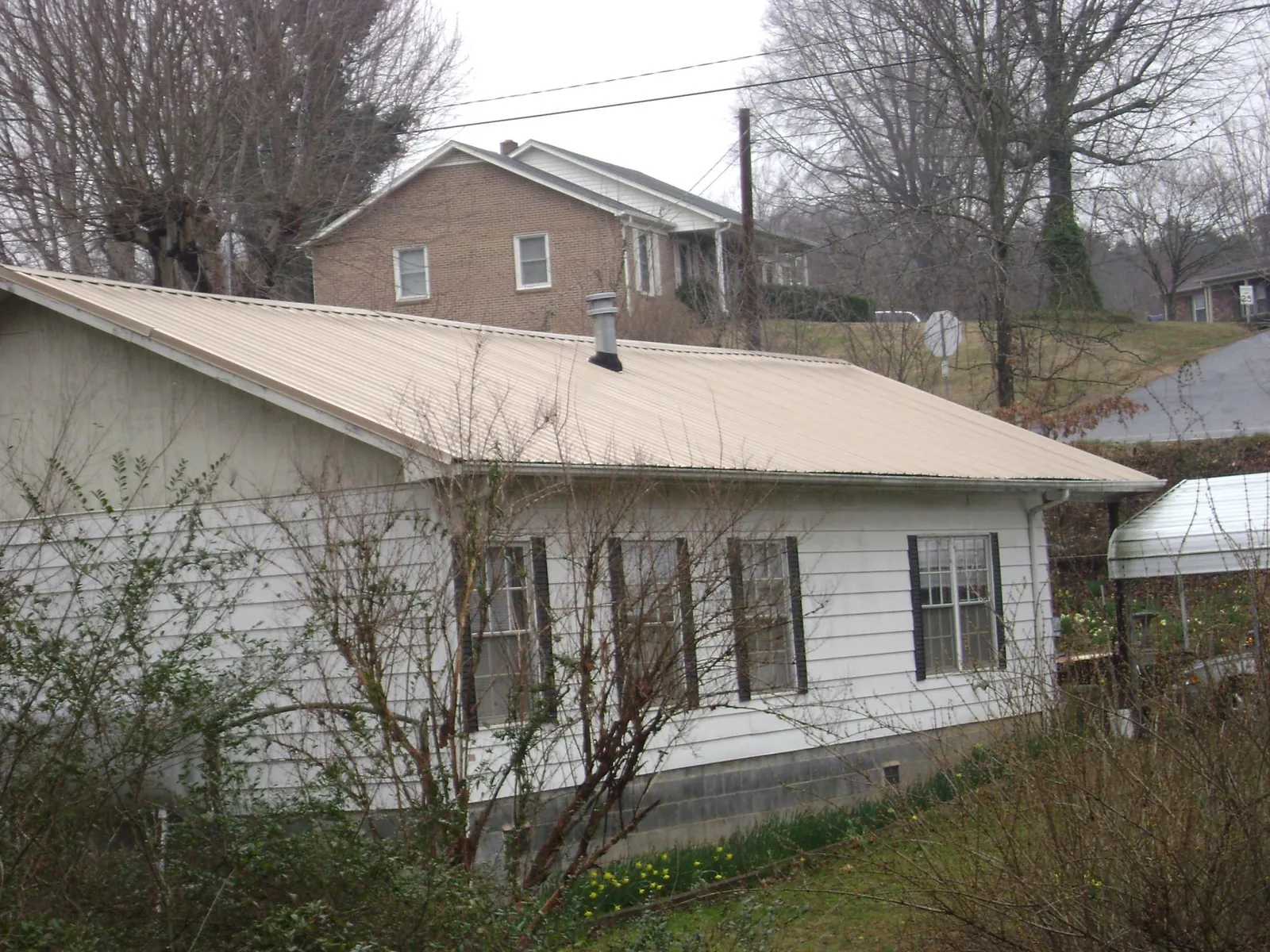 Tan metal roof on a white sided house set into a hillside — Commercial Roofing by Roofing Brothers in Saint Paul Park